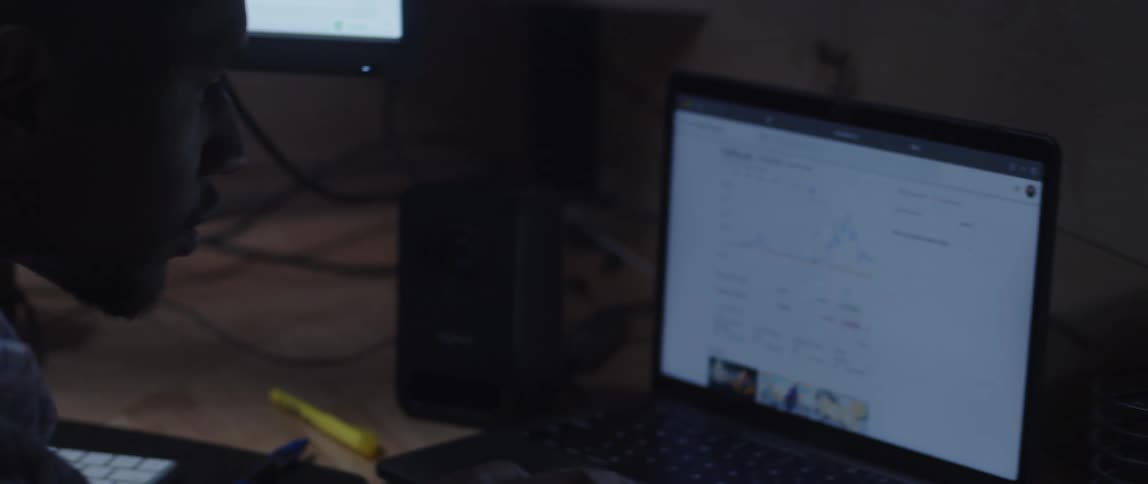 A man looking intently at his laptop screen that sits on his desk with pens around