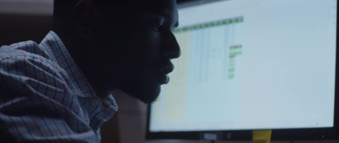 A man's face up close looking contemplatively with a computer screen in the background