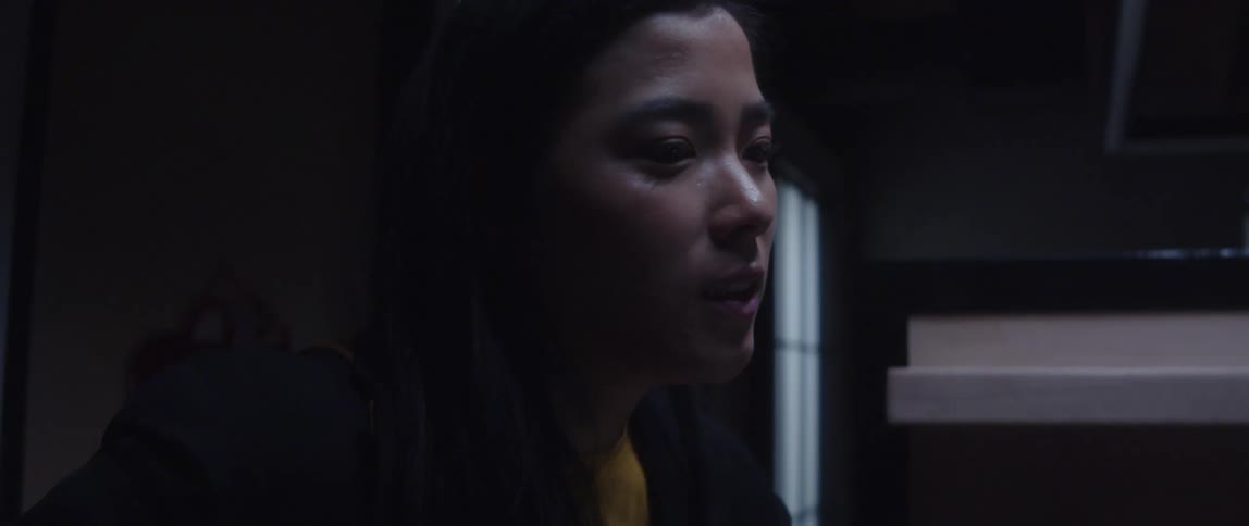Light shines on a woman's face as she shakes her head and smiles as she speaks to someone off screen