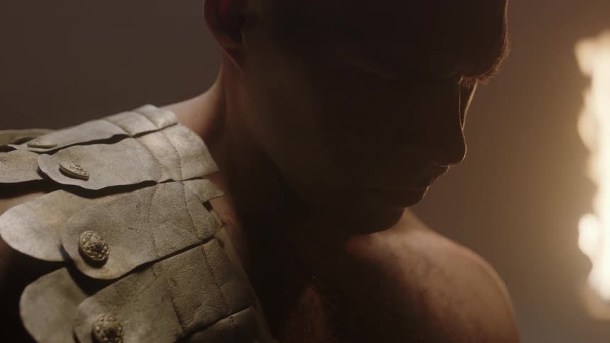 A man is looking down as a fire flickers behind