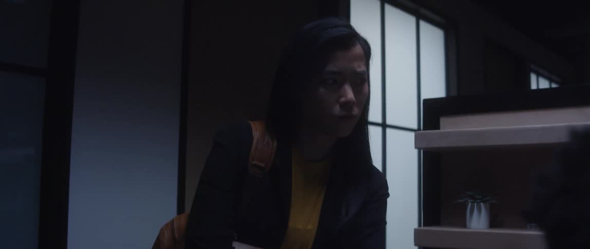 A man is sitting at a desk and a woman is standing behind him next to a shelf as she looks over his head