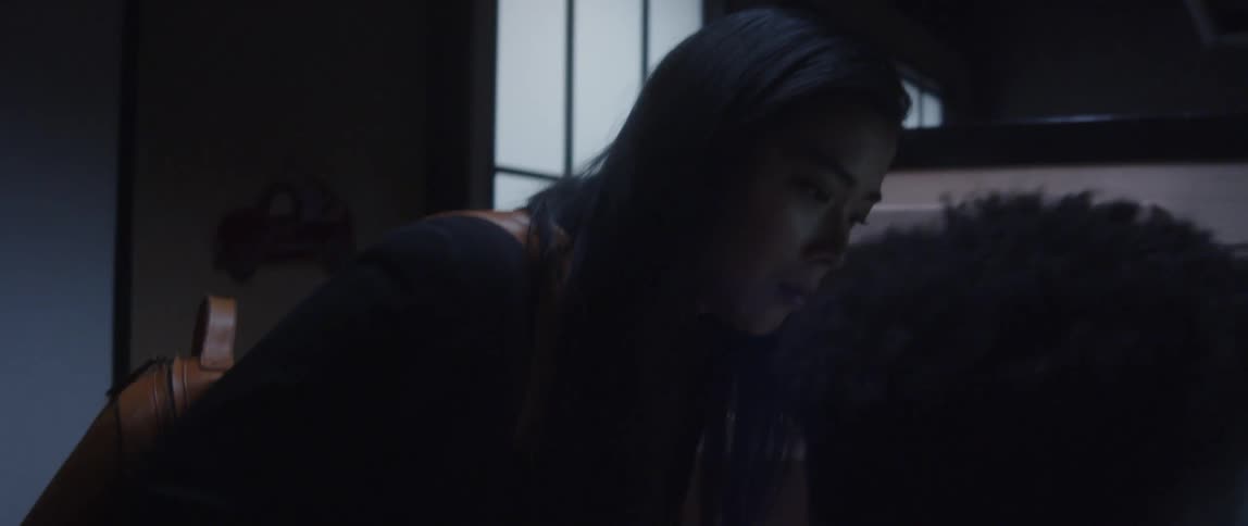Businesswoman with black jacket and brown backpack leans over desk next to man using computer in the office
