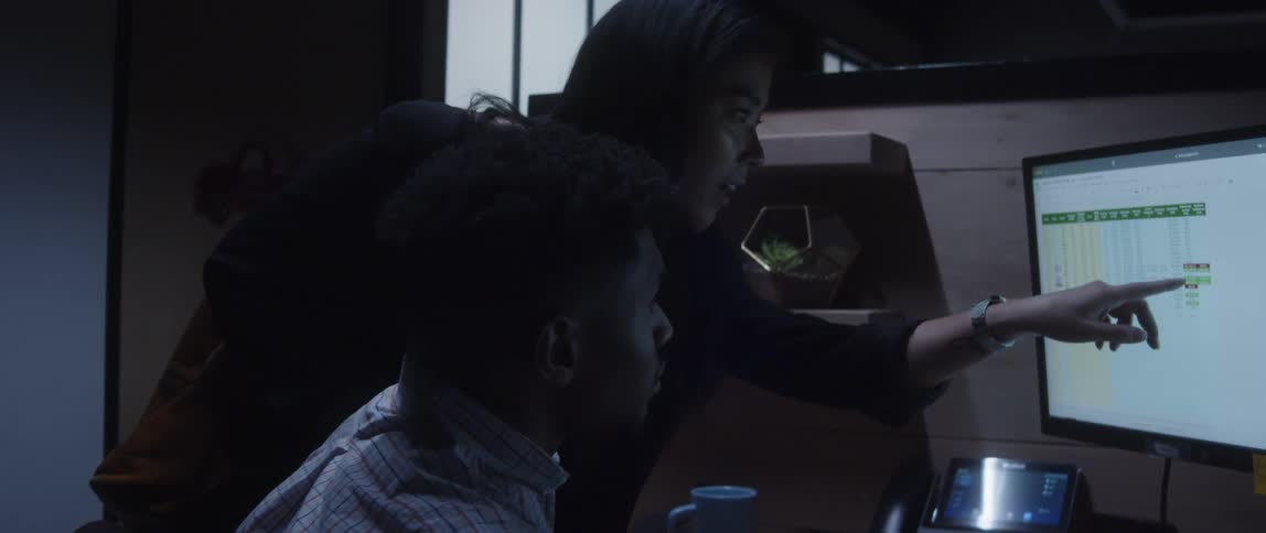 Businessman sits at desk and businesswoman points at computer screen at the office