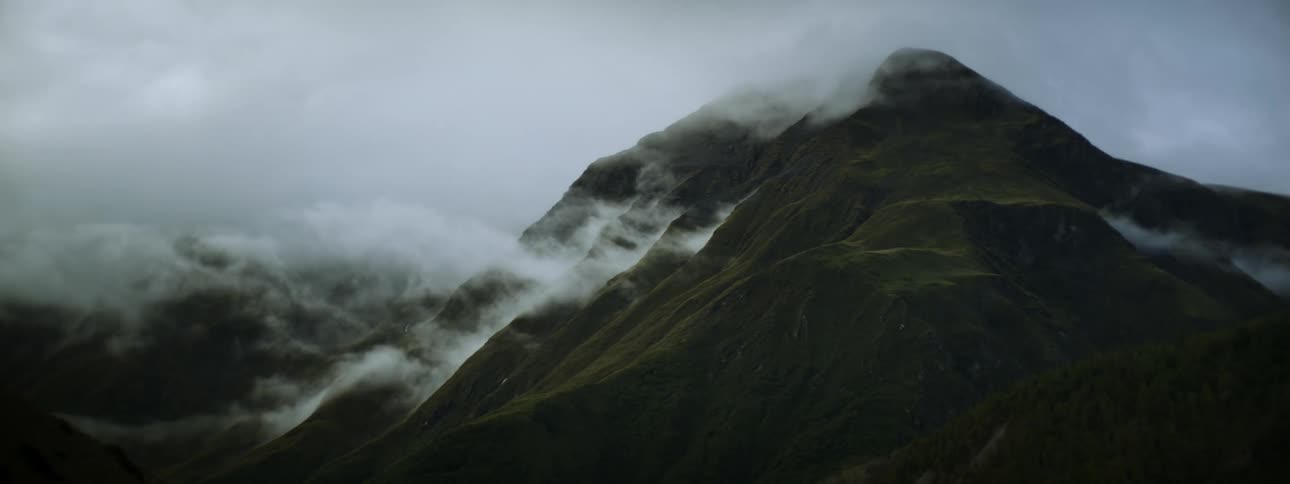 Mountains peak high in a cloudy sky as fog rolls on the mountainside