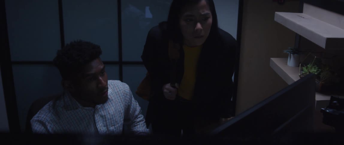 Businessman sitting at desk talks to businesswoman looking at computer screen at the office
