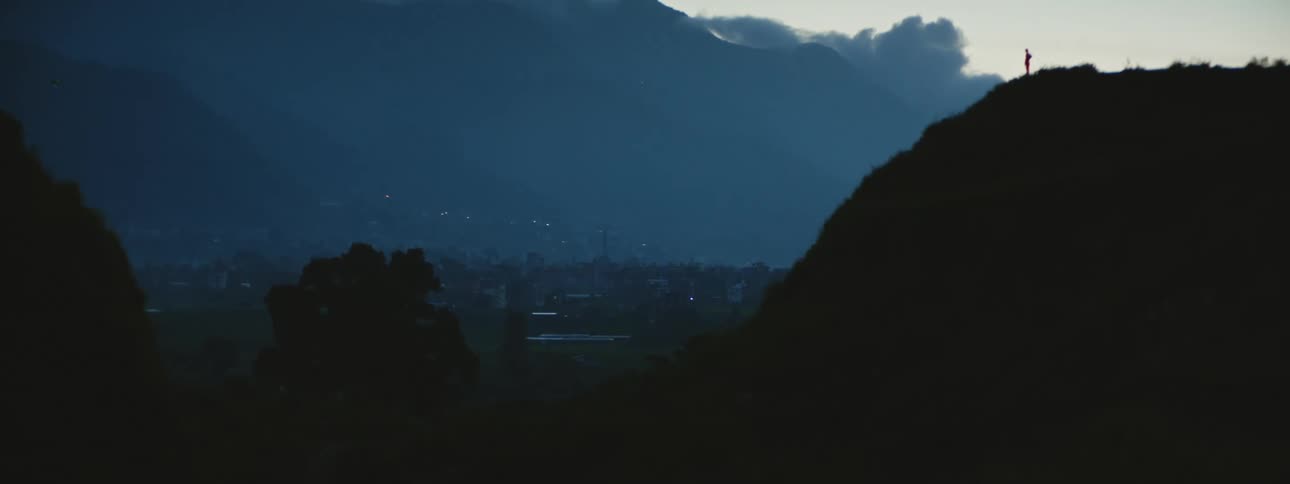 Distant person standing on the edge of mountain is silhouetted against the sky