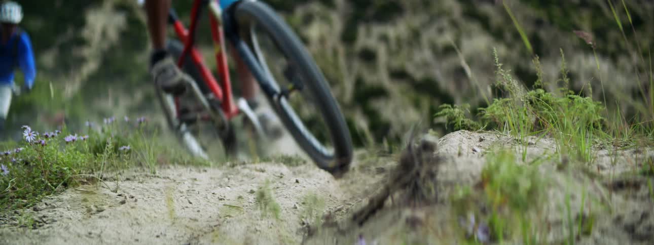 Two men ride bicycles on dirt track in the field