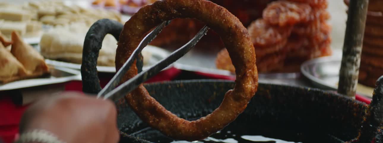 An adult is holding a giant dough over a kettle of frying oil