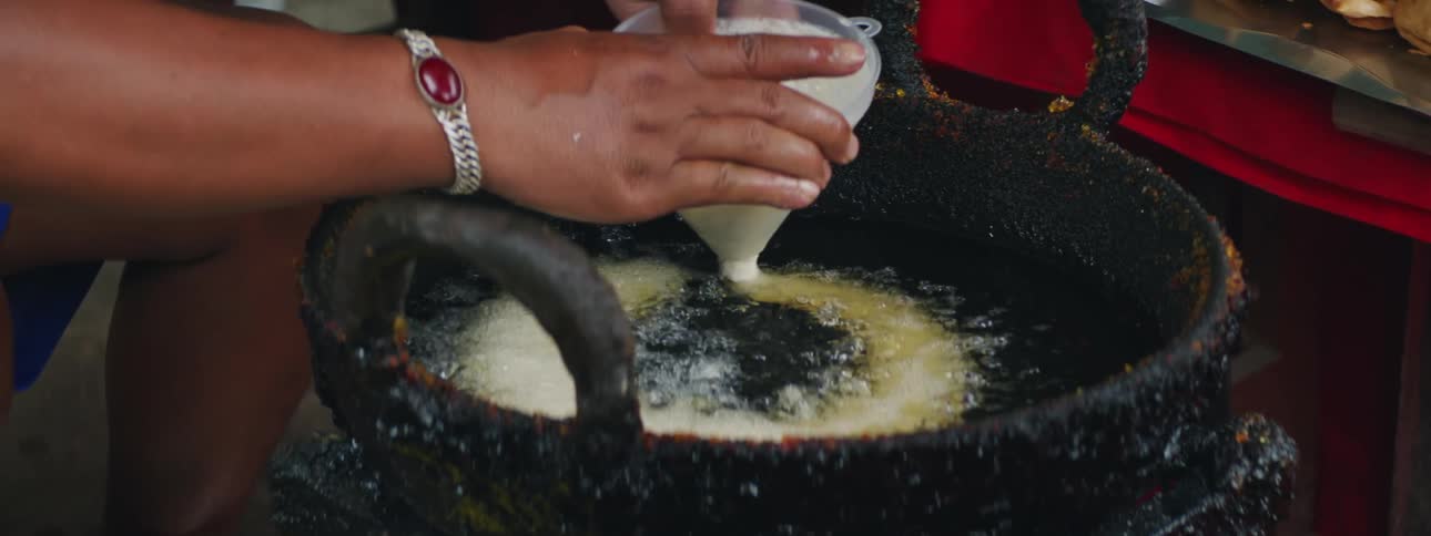 Woman uses a funnel to pour batter into a pan with hot oil