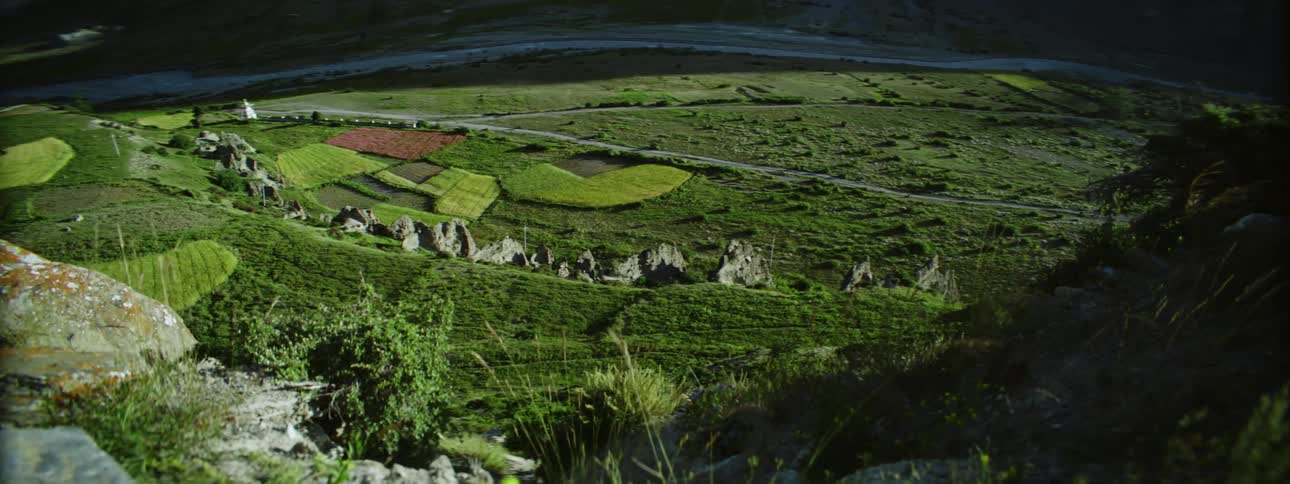Panoramic view of an extensive green field with farms seen from a mountain at daytime