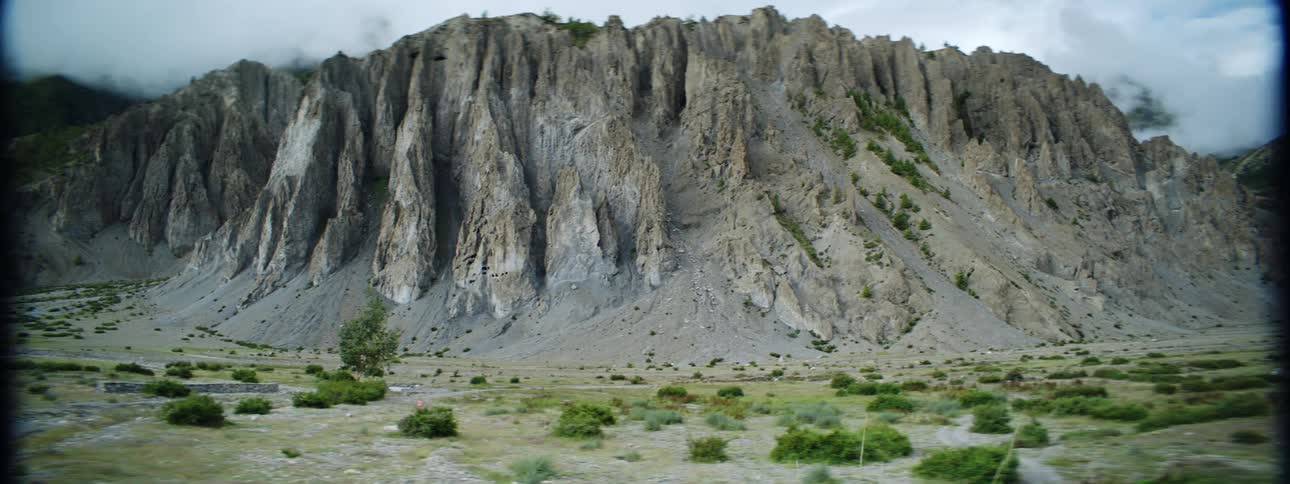 A mountain with sparse grass on its slopes and a woman running towards it