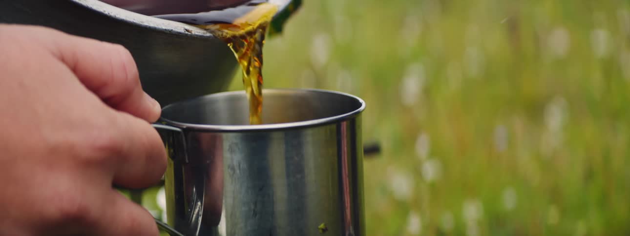 Outdoor Tea Pouring: Hands Filling Stainless Steel Cups at a Campsite