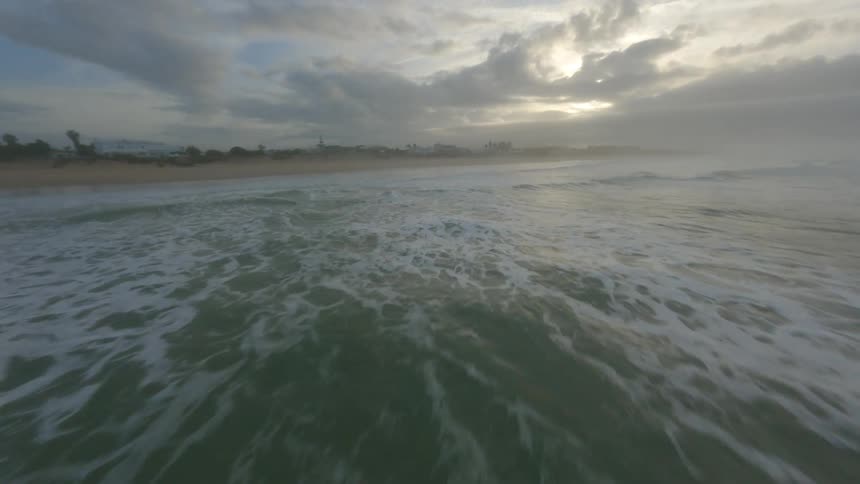 Aerial view of foamy ocean waves breaking against the beach