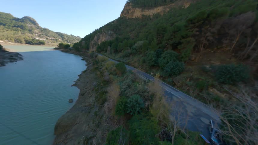 A turquoise river runs through a deep wooded gorge with a narrow highway next to it