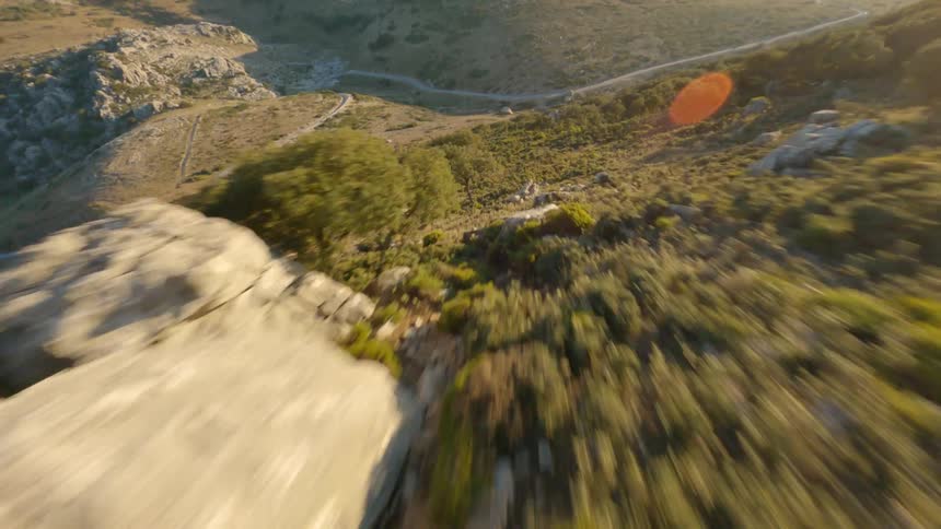 Drone flying near crags before descending down into a grass and tree like area