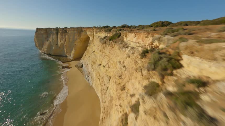 Bright sun shines onto cliffs and narrow beach bordering blue green water