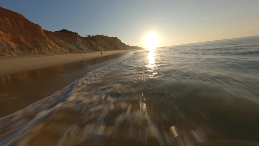 Dynamic drone footage flying close to the coastline of a beach next to a cliff at evening
