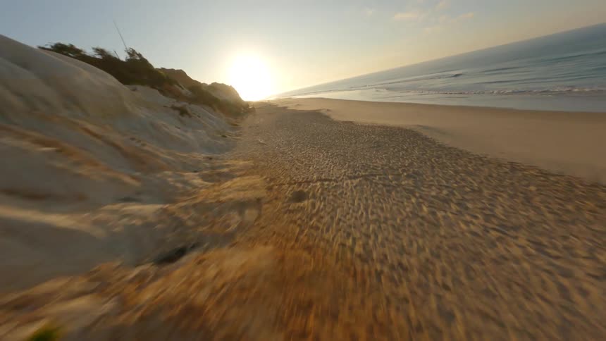 Aerial view of long beach between cliff and ocean at sunset