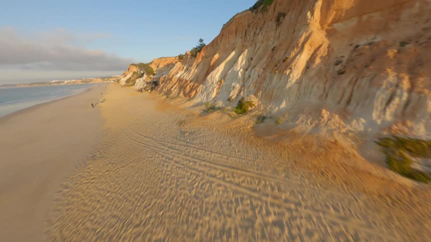 Dynamic drone footage flying close to the coastline of a beach next to a cliff at evening