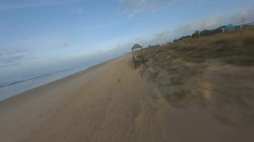 Automobiles travel on a street in a community along the coast as a man stands on the beach as the waves roll in to shore