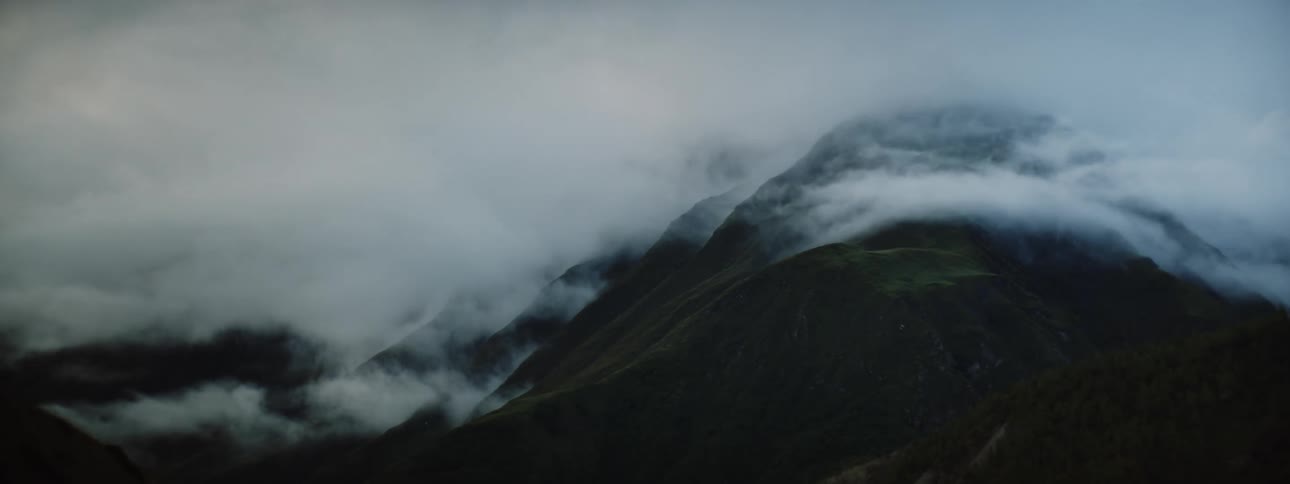 Mountains peak high in a cloudy sky as fog rolls on the mountainside