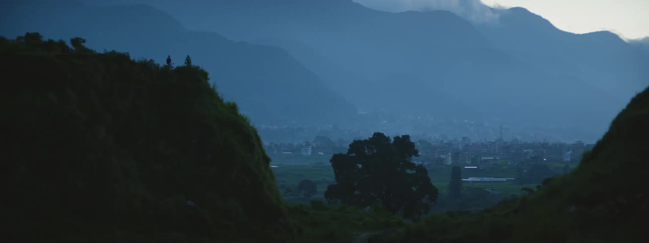 People stand on the edge of cliff against the city skyline at dusk