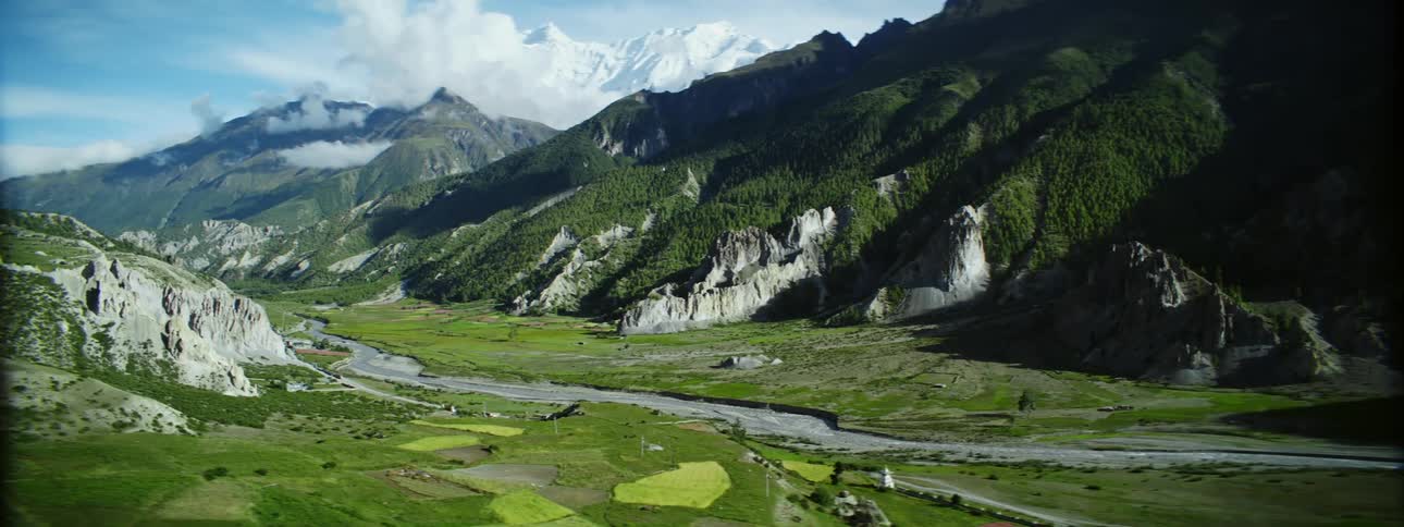 Farm fields fill valley near one side of river across from forest covered mountain