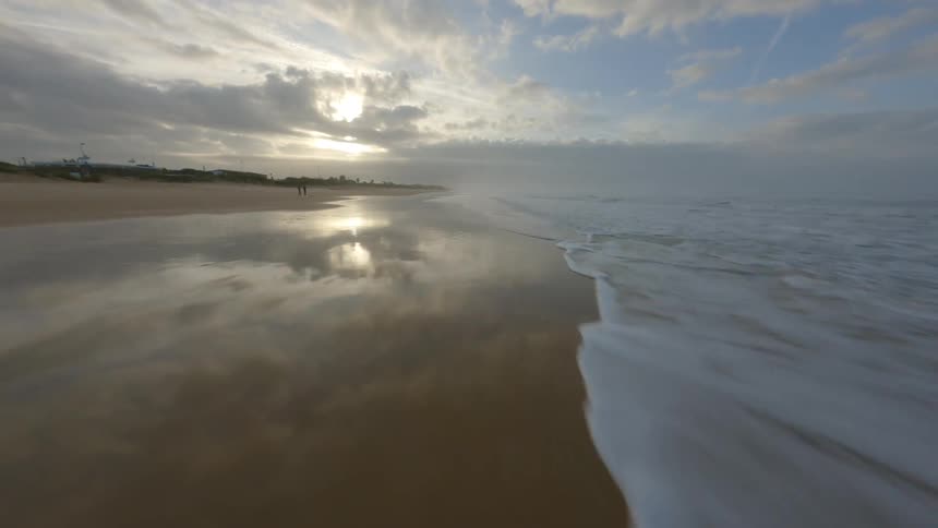 Dynamic drone footage flying close to the coastline of a beach next to a neighborhood at evening