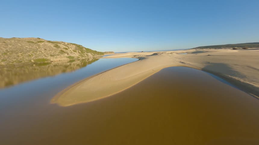 A river winds around a beach along the coast