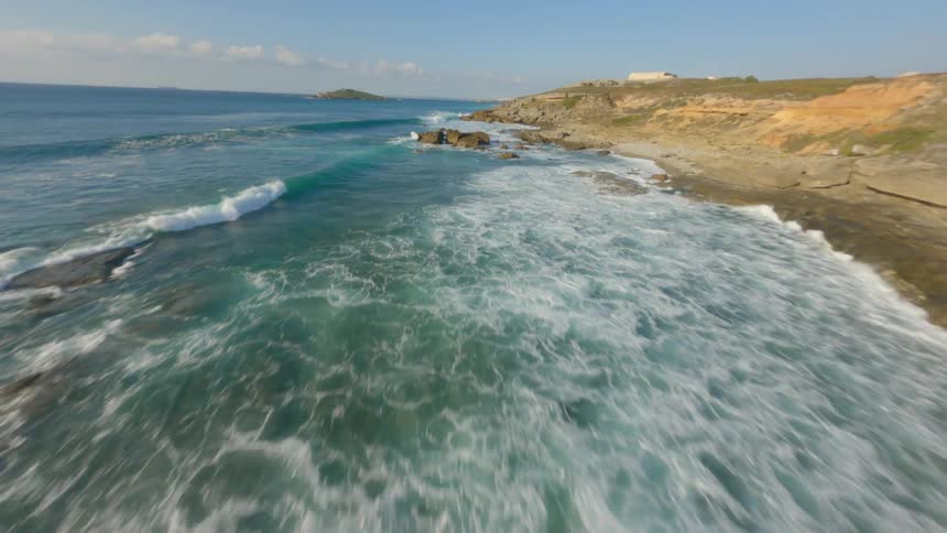 A sped up aerial view of waves crashing against the coast line of rocks and bouldersrevealing buildings on the coast landing