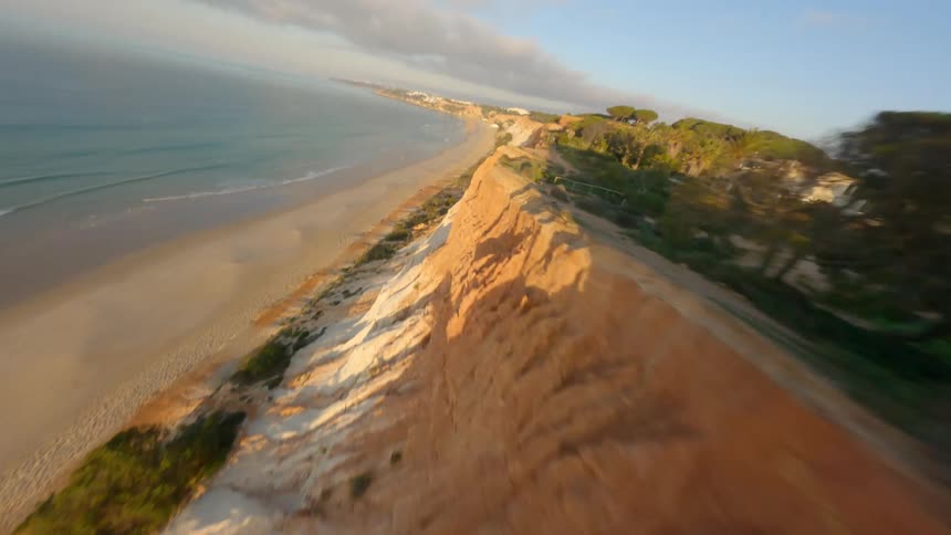 Dynamic drone footage flying close to the coastline of a beach next to a cliff at evening