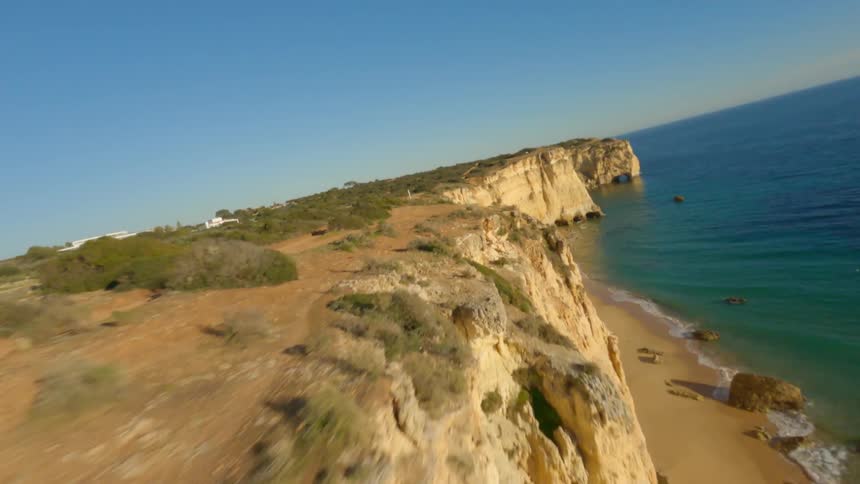 Large white homes sit a distance from cliffs and narrow beach bordering blue green water