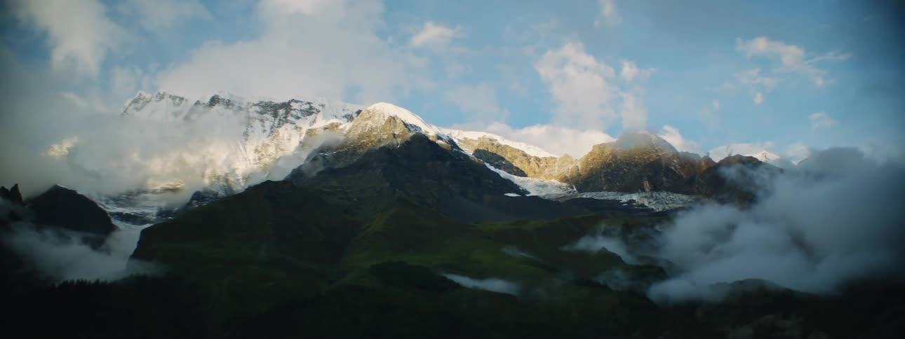 Dense clouds settle above the peaks of snow capped mountains