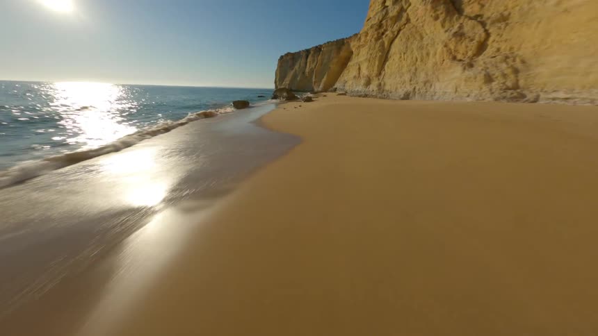 An aerial view of a coastline cliff with waves crashing against the sandy beach