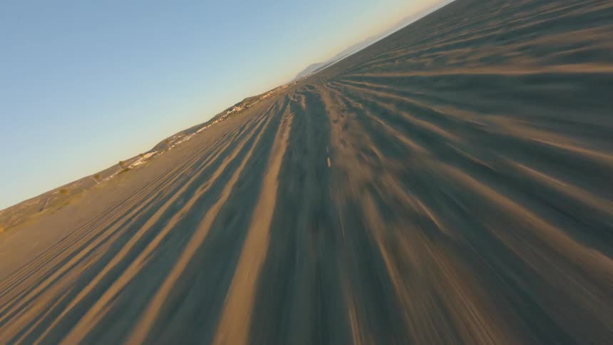 Moving across a beach with a community along the coast and mountains in the distance