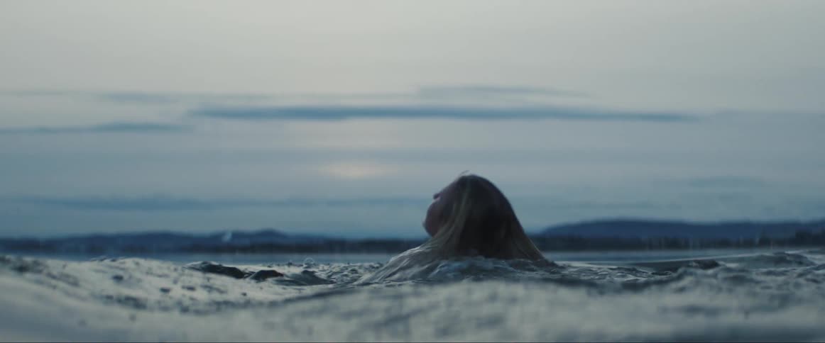 Blonde woman with swimsuit swims in sea at dusk