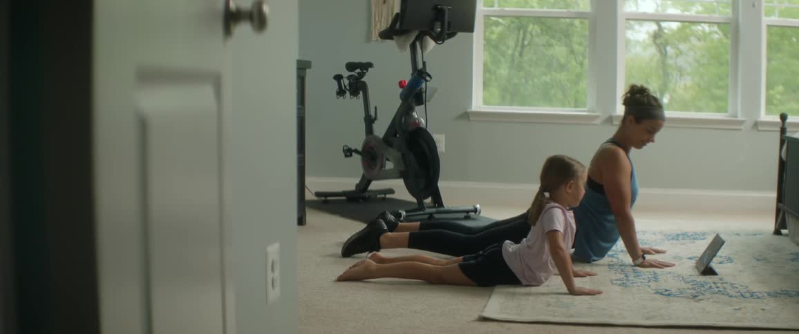 A woman and a girl on a bedroom floor exercising in front of a tablet