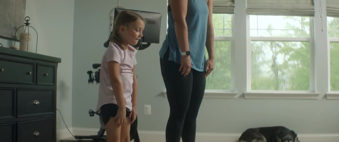 Mom and daughter bend over and stretch to exercise in a room indoors