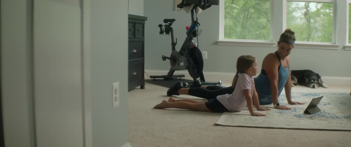 A woman and a female child do yoga in a room in front of a tablet