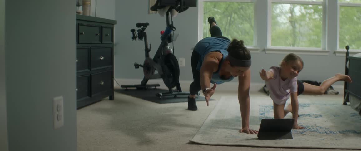 A woman and her daughter stretch in an exercise pose with a tablet in front of them