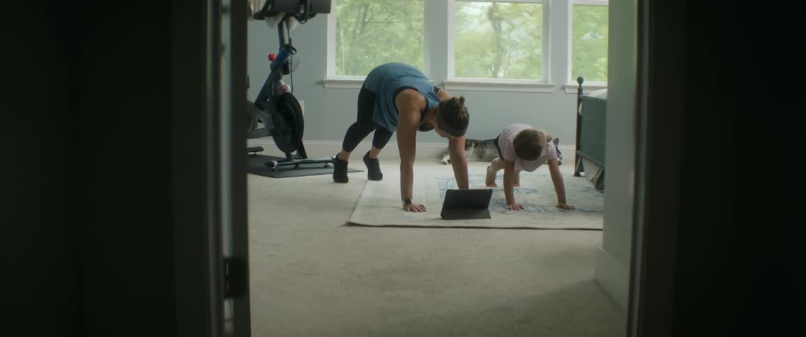 Mother smiling at her daughter as they stretch and exercise together in a bedroom