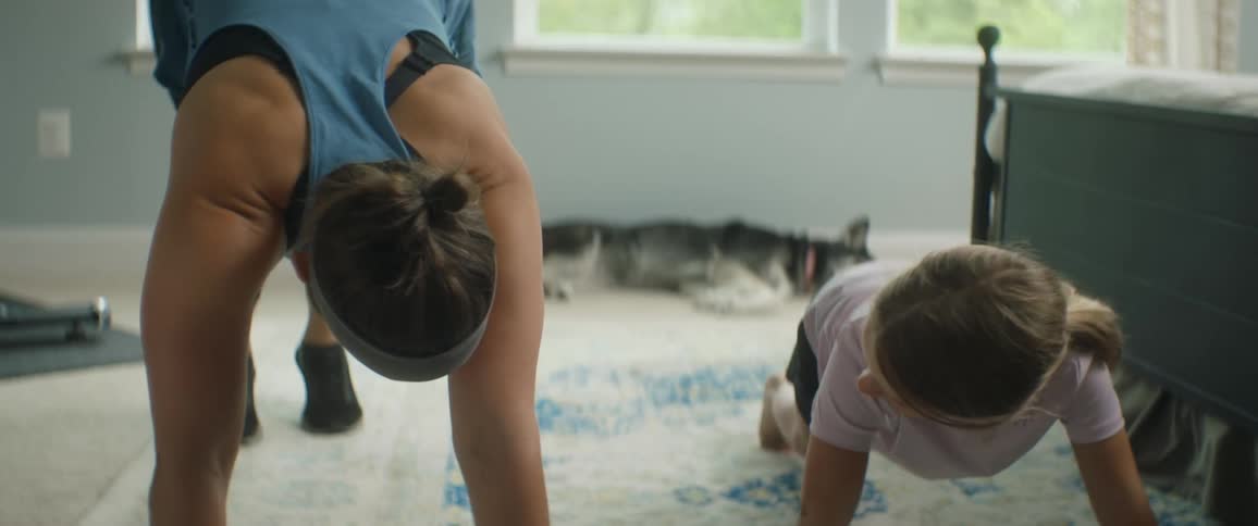 A woman does yoga at home and her daughter follows along with her