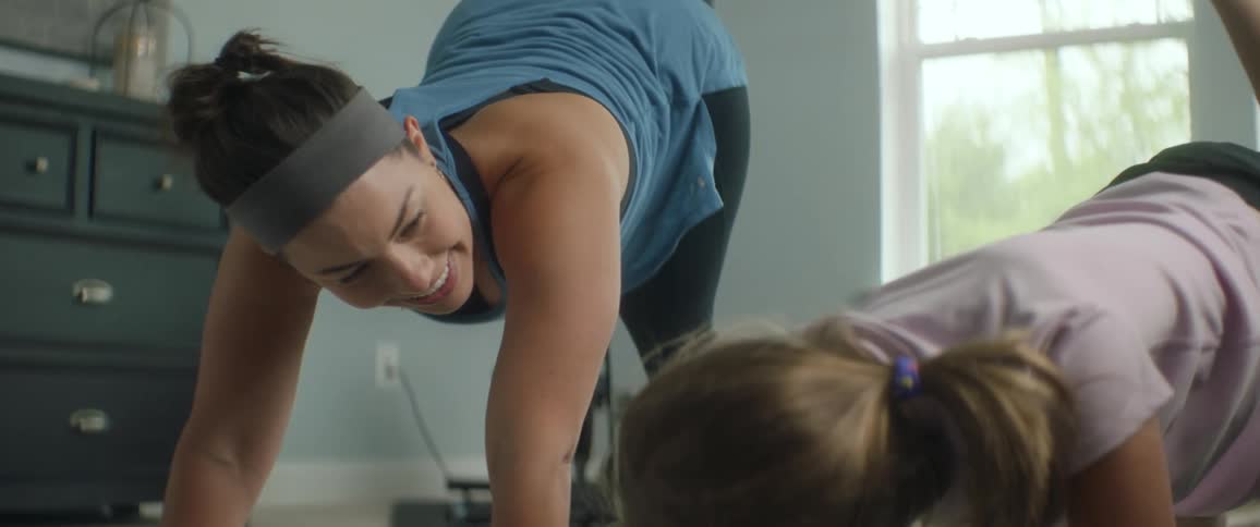 Mother smiles at her child as they exercise together inside of a house