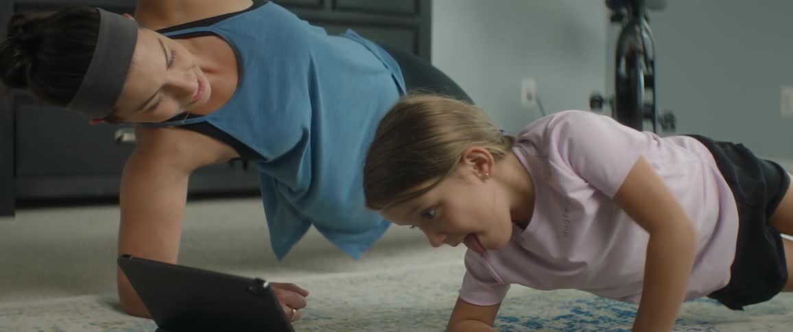 A woman and child do yoga together while looking at a tablet on the floor