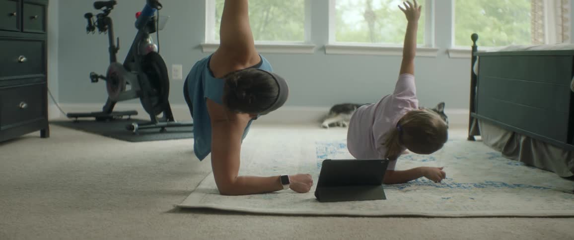 A woman and her daughter do stretching exercises on the bedroom floor