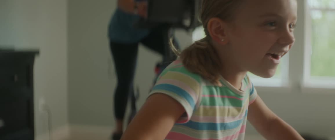 A girl in a room laughing with a woman on an exercise bike in the background