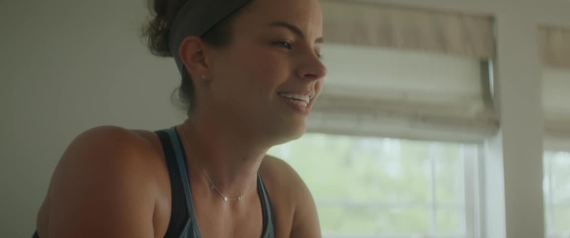 A woman exercises on a stationary bike indoors while she smiles