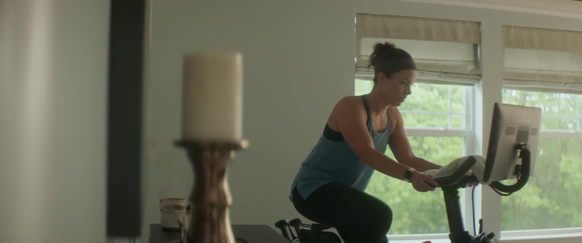 Woman exercises on stationary bicycle next to windows