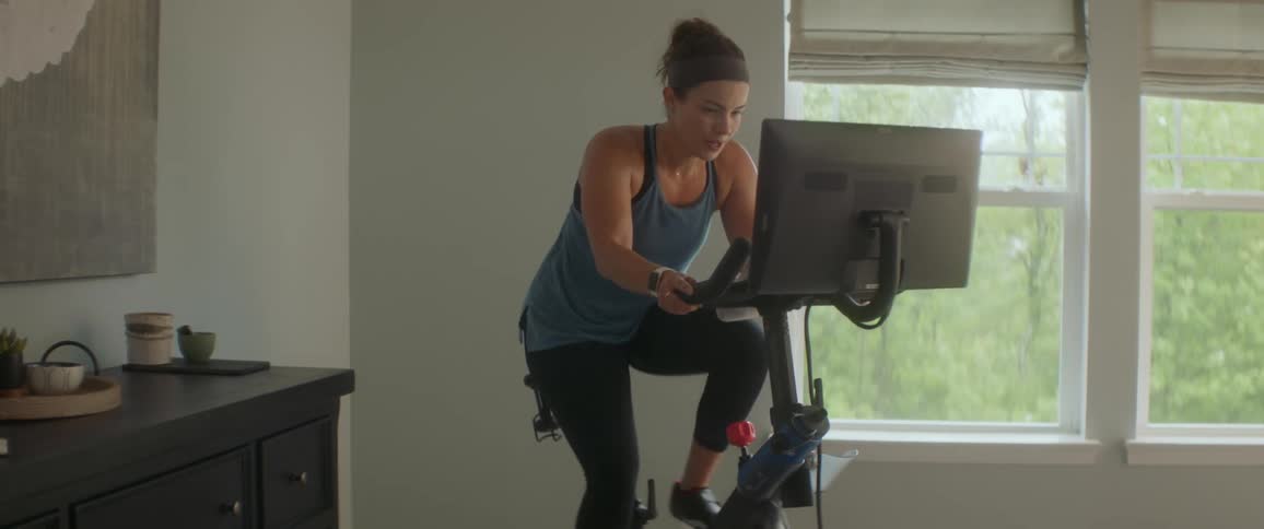 Woman on a stationary bike inside of a house peddling quickly