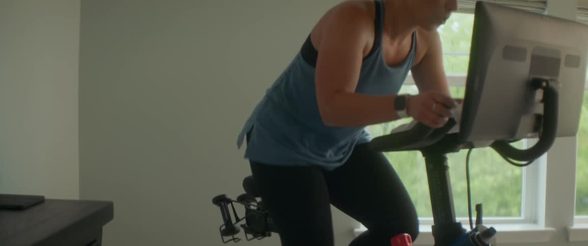 A woman in a room exercising on a exercise bike with a window in the background